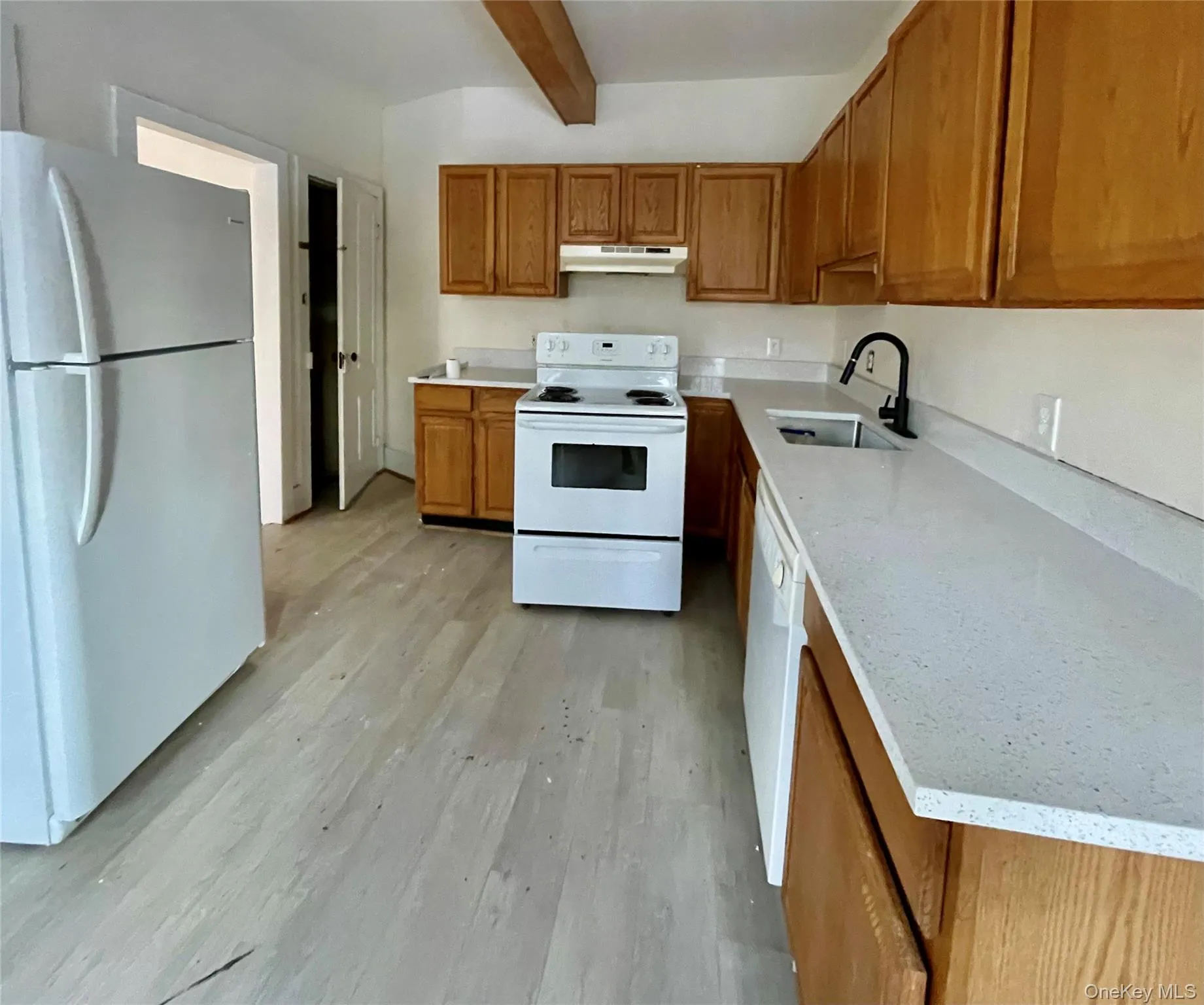 Kitchen with white appliances, brown cabinets, beamed ceiling, light wood-style flooring, and under cabinet range hood Kitchen with white appliances, brown cabinets, beamed ceiling, light wood-style flooring, and under cabinet range hood
