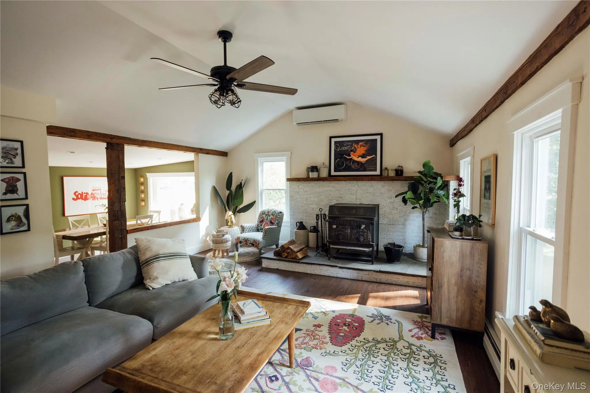 Living room featuring ceiling fan, wood finished floors, lofted ceiling, an AC wall unit, and a wood stove Living room featuring ceiling fan, wood finished floors, lofted ceiling, an AC wall unit, and a wood stove