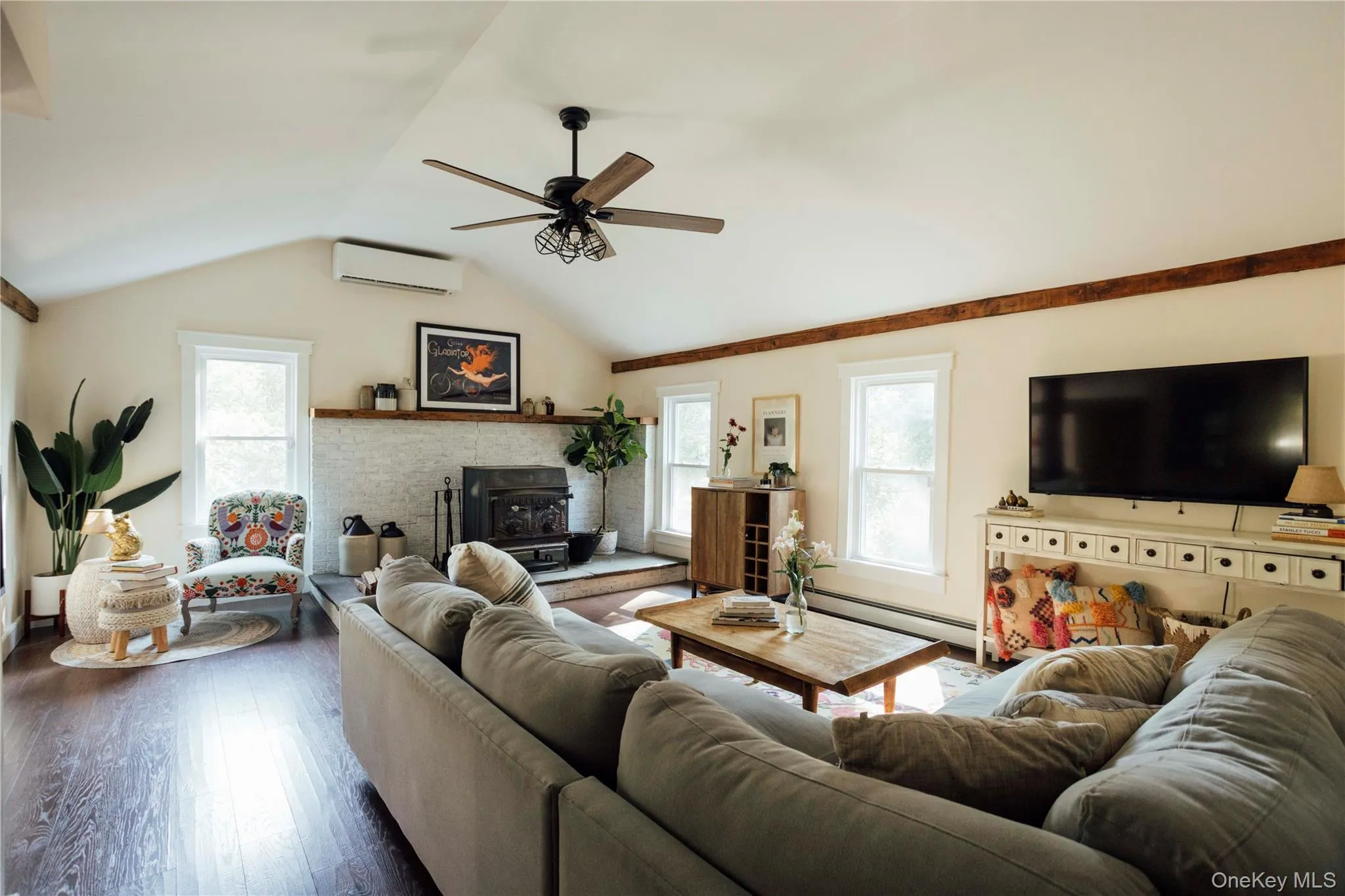 Living room featuring a wood stove, lofted ceiling, a ceiling fan, dark wood-type flooring, and baseboard heating Living room featuring a wood stove, lofted ceiling, a ceiling fan, dark wood-type flooring, and baseboard heating
