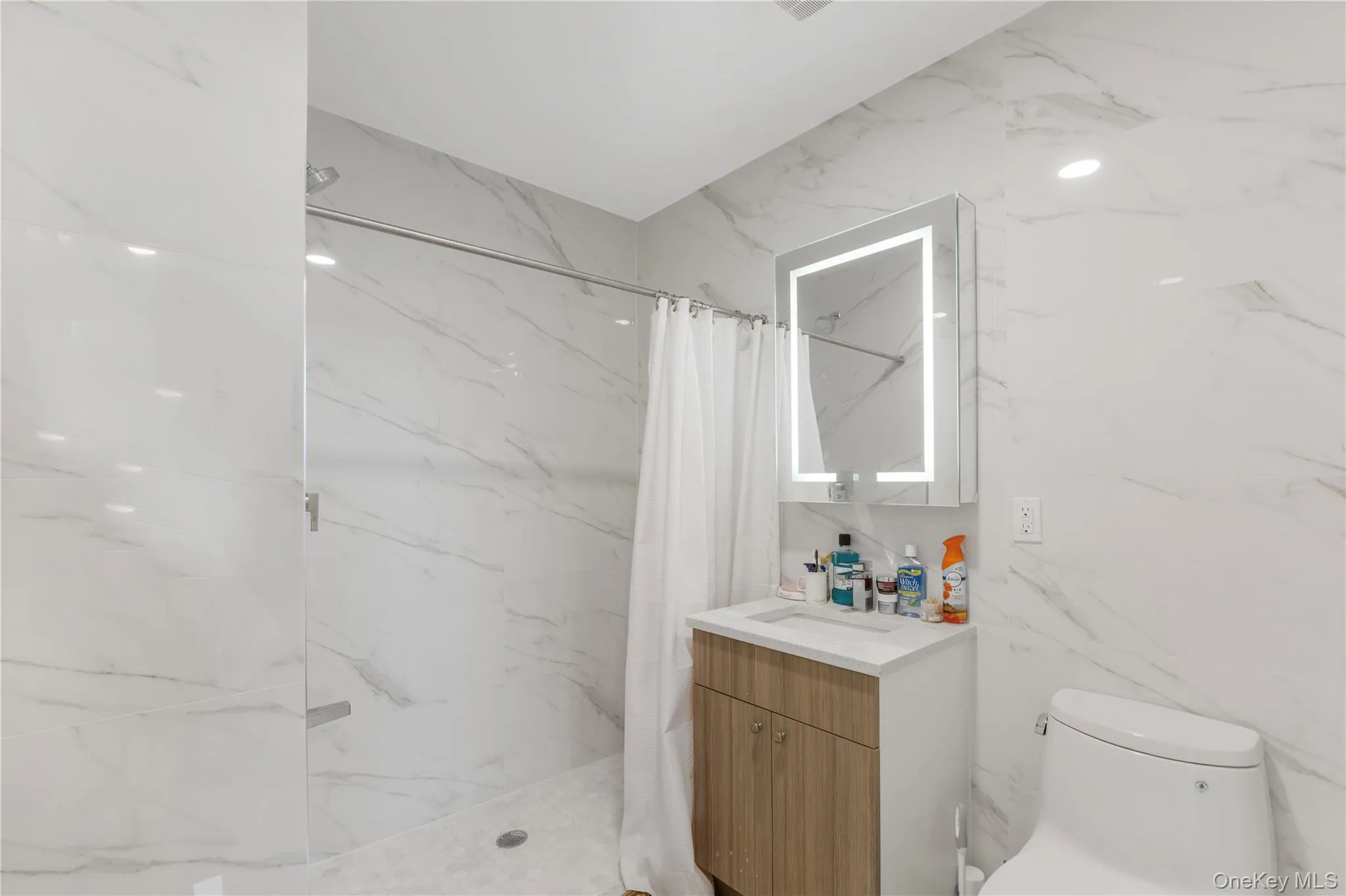 Bathroom featuring vanity, a marble finish shower, and stone wall Bathroom featuring vanity, a marble finish shower, and stone wall