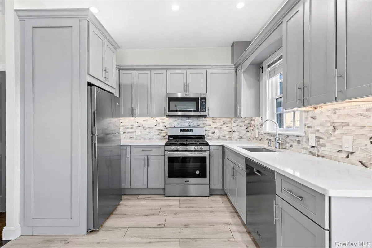 Kitchen featuring gray cabinetry, appliances with stainless steel finishes, tasteful backsplash, a wall mounted air conditioner, and light wood-style floors Kitchen featuring gray cabinetry, appliances with stainless steel finishes, tasteful backsplash, a wall mounted air conditioner, and light wood-style floors