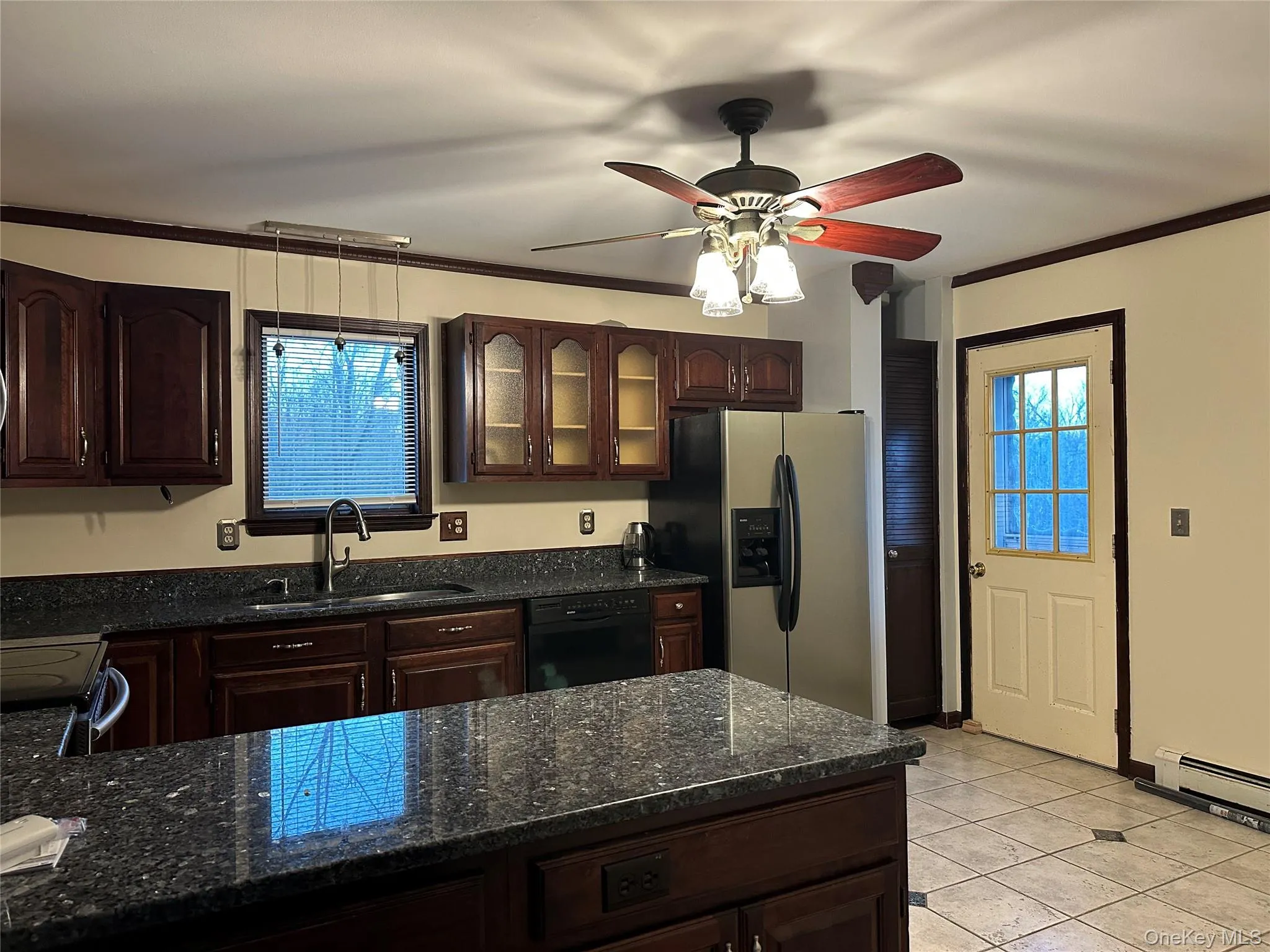Kitchen with dark brown cabinets, dark stone countertops, ornamental molding, stainless steel fridge with ice dispenser, and glass insert cabinets Kitchen with dark brown cabinets, dark stone countertops, ornamental molding, stainless steel fridge with ice dispenser, and glass insert cabinets