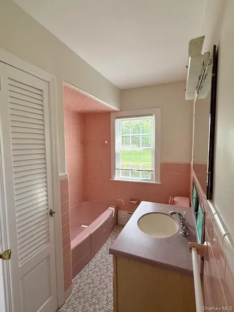 Full bathroom featuring vanity, shower combination, tile walls, and a wainscoted wall Full bathroom featuring vanity, shower combination, tile walls, and a wainscoted wall