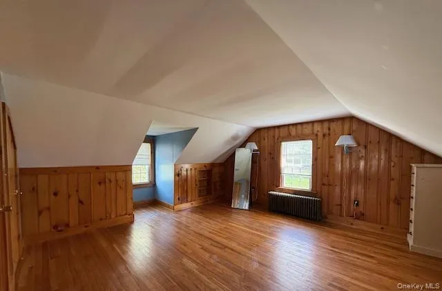 Bonus room featuring vaulted ceiling, light wood-style floors, radiator, and wood walls Bonus room featuring vaulted ceiling, light wood-style floors, radiator, and wood walls