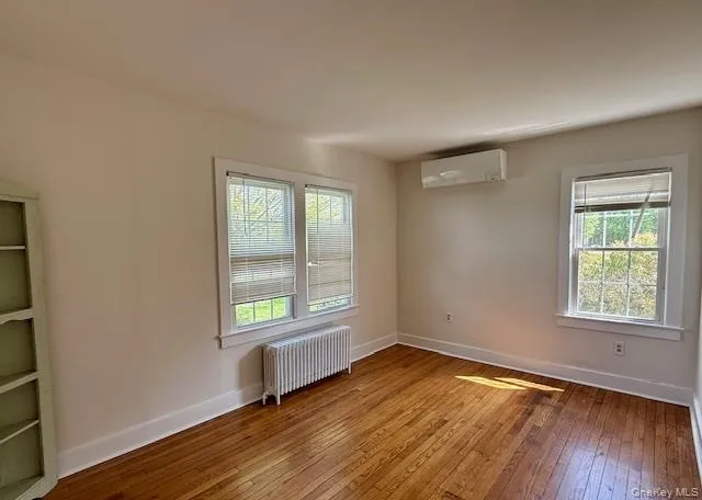 Spare room with radiator, hardwood / wood-style floors, and healthy amount of natural light Spare room with radiator, hardwood / wood-style floors, and healthy amount of natural light