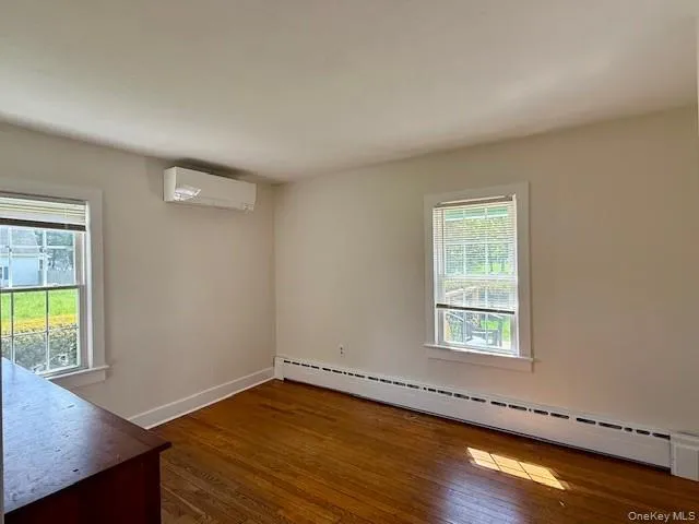 Unfurnished room with a baseboard radiator, dark wood-type flooring, a wall mounted AC, and plenty of natural light Unfurnished room with a baseboard radiator, dark wood-type flooring, a wall mounted AC, and plenty of natural light