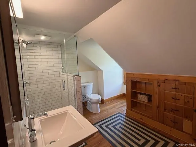 Bathroom featuring wood finished floors, vaulted ceiling, and a stall shower Bathroom featuring wood finished floors, vaulted ceiling, and a stall shower