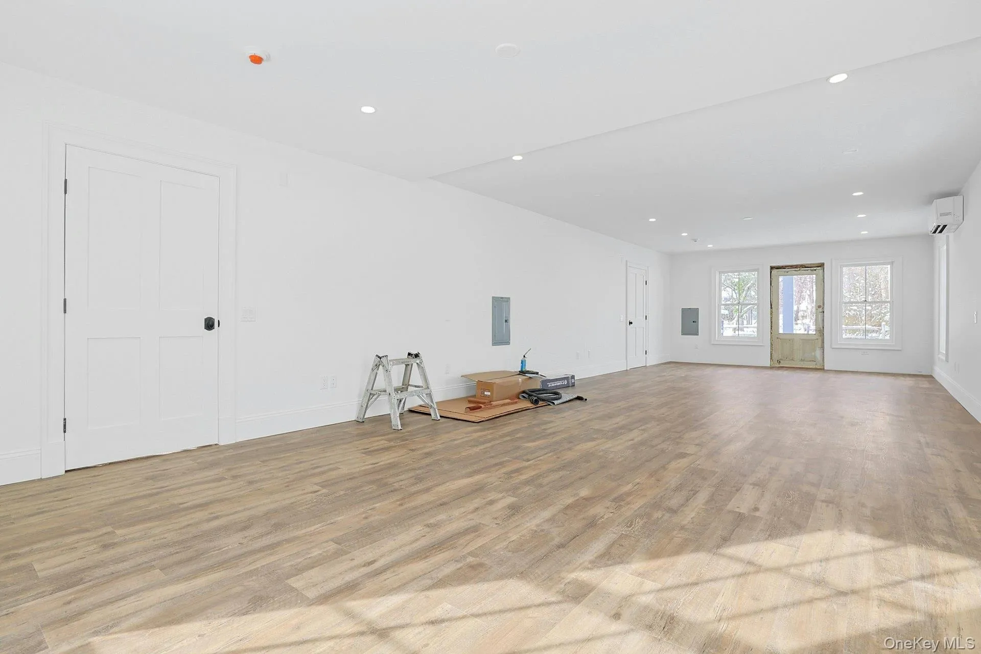 Unfurnished living room with light wood-style floors, recessed lighting, electric panel, and a wall unit AC Unfurnished living room with light wood-style floors, recessed lighting, electric panel, and a wall unit AC