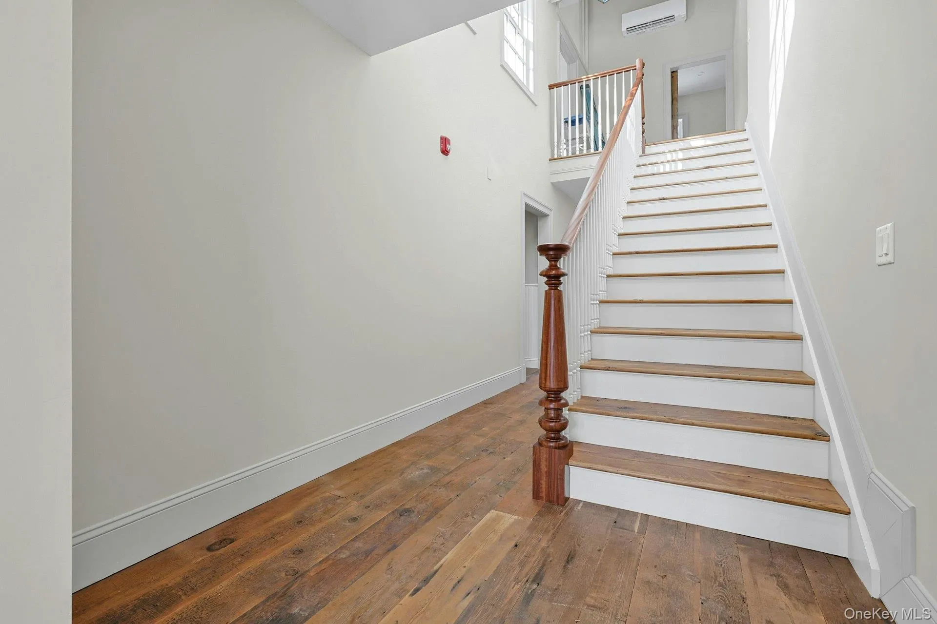 Stairway with hardwood / wood-style floors, a wall mounted AC, and a high ceiling Stairway with hardwood / wood-style floors, a wall mounted AC, and a high ceiling