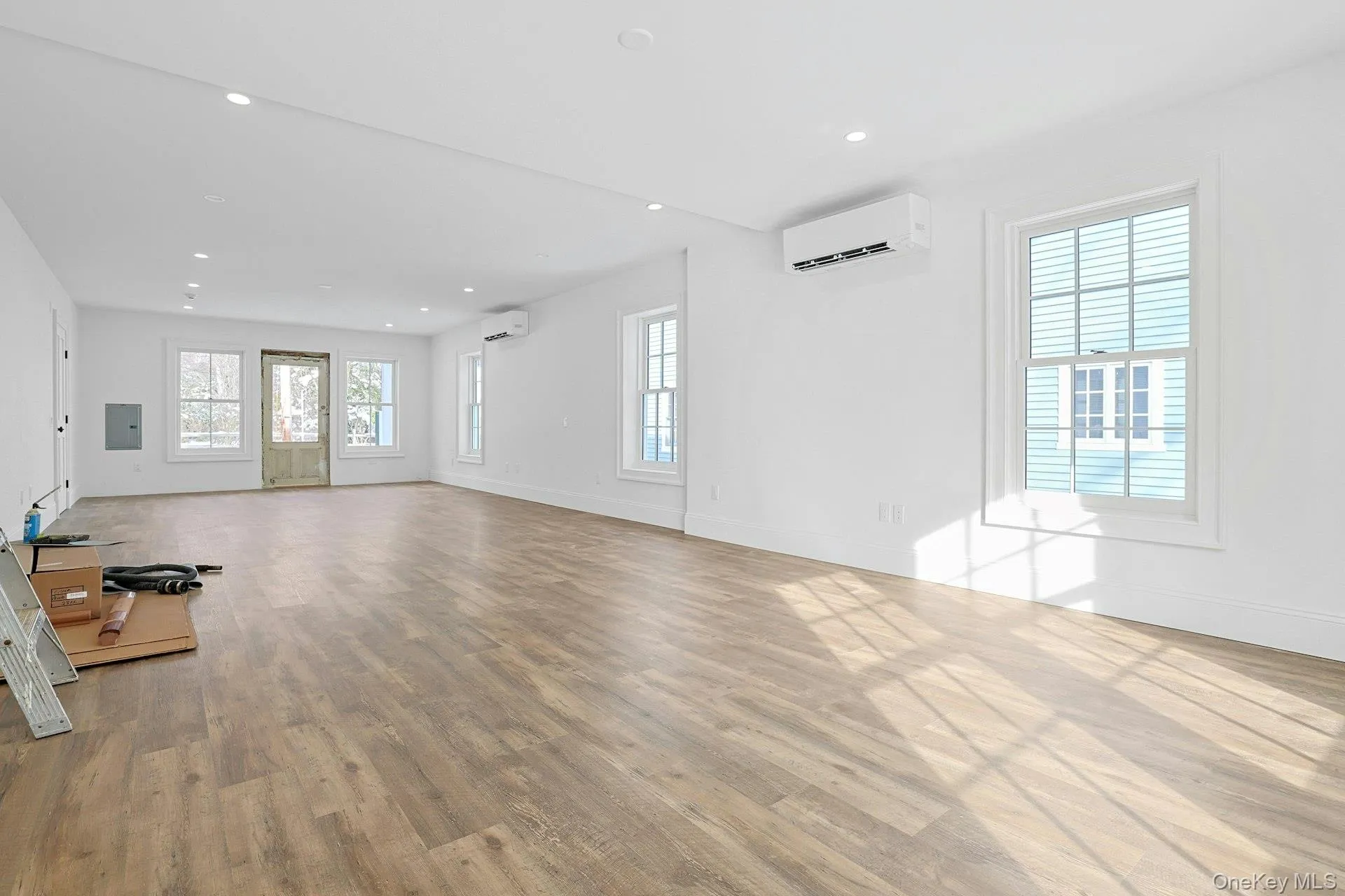 Unfurnished living room with light wood finished floors, an AC wall unit, recessed lighting, and electric panel Unfurnished living room with light wood finished floors, an AC wall unit, recessed lighting, and electric panel