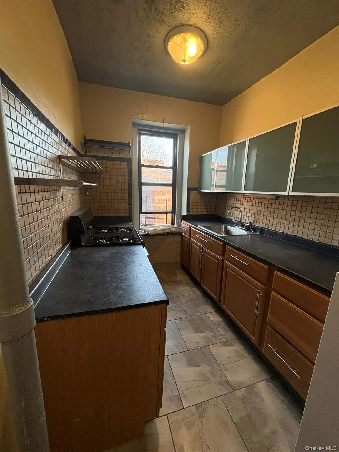 Kitchen with dark countertops, decorative backsplash, black gas range, a textured ceiling, and brown cabinets Kitchen with dark countertops, decorative backsplash, black gas range, a textured ceiling, and brown cabinets