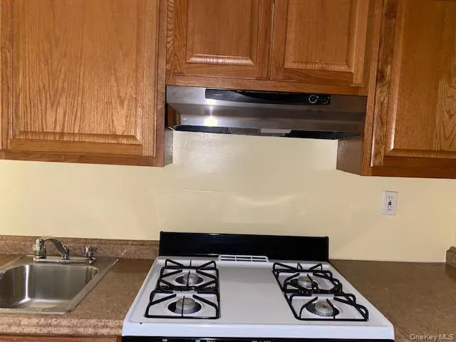 Kitchen featuring gas range gas stove, ventilation hood, brown cabinetry, and dark countertops Kitchen featuring gas range gas stove, ventilation hood, brown cabinetry, and dark countertops