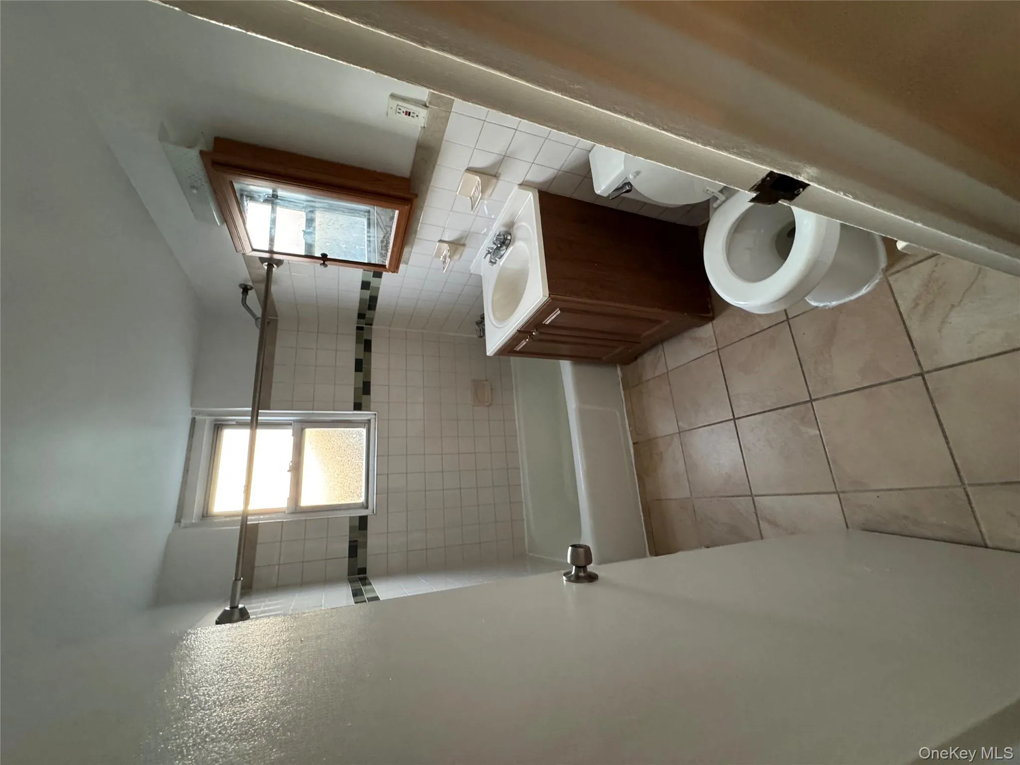 Full bath featuring vanity, plenty of natural light, washtub / shower combination, light tile patterned floors, and tile walls Full bath featuring vanity, plenty of natural light, washtub / shower combination, light tile patterned floors, and tile walls