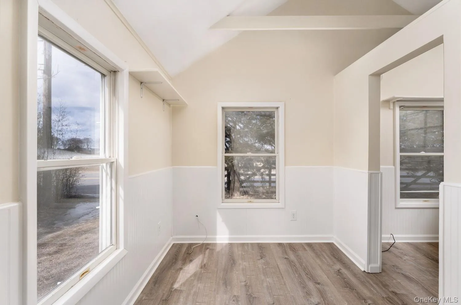 Spare room featuring wainscoting, vaulted ceiling, and wood finished floors Spare room featuring wainscoting, vaulted ceiling, and wood finished floors