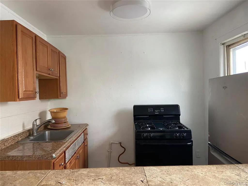Kitchen featuring gas stove, brown cabinetry, and freestanding refrigerator Kitchen featuring gas stove, brown cabinetry, and freestanding refrigerator