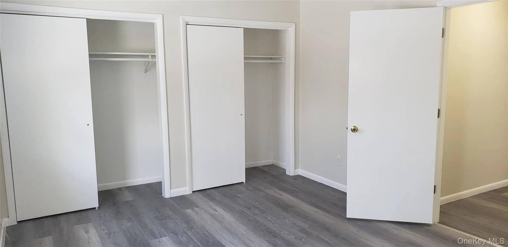 Unfurnished bedroom featuring multiple closets and dark wood-style flooring Unfurnished bedroom featuring multiple closets and dark wood-style flooring