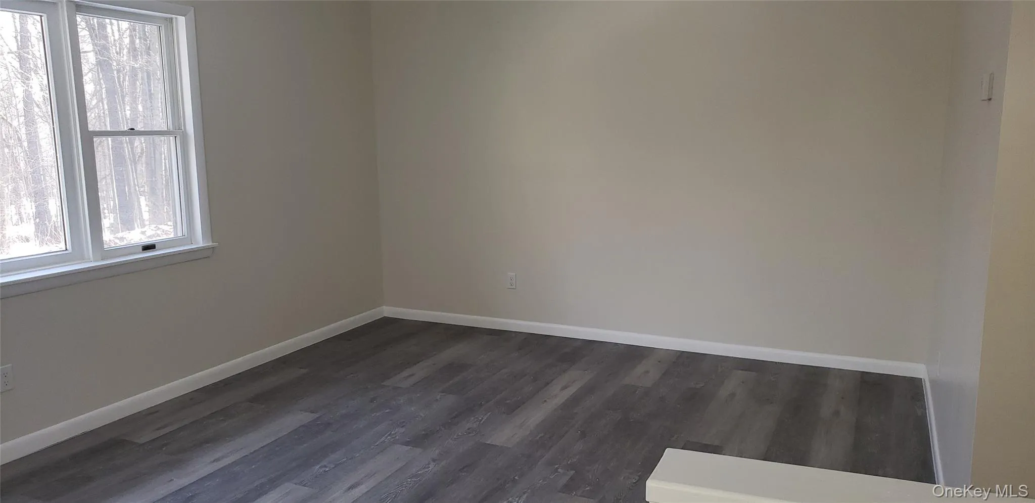Empty room with dark wood-type flooring and baseboards Empty room with dark wood-type flooring and baseboards