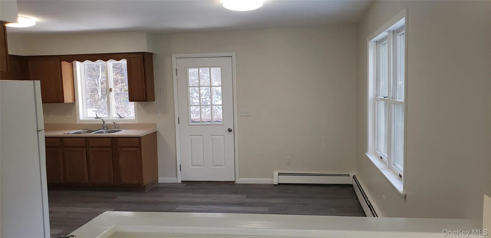 Kitchen featuring freestanding refrigerator, light countertops, brown cabinetry, a baseboard radiator, and dark wood finished floors Kitchen featuring freestanding refrigerator, light countertops, brown cabinetry, a baseboard radiator, and dark wood finished floors