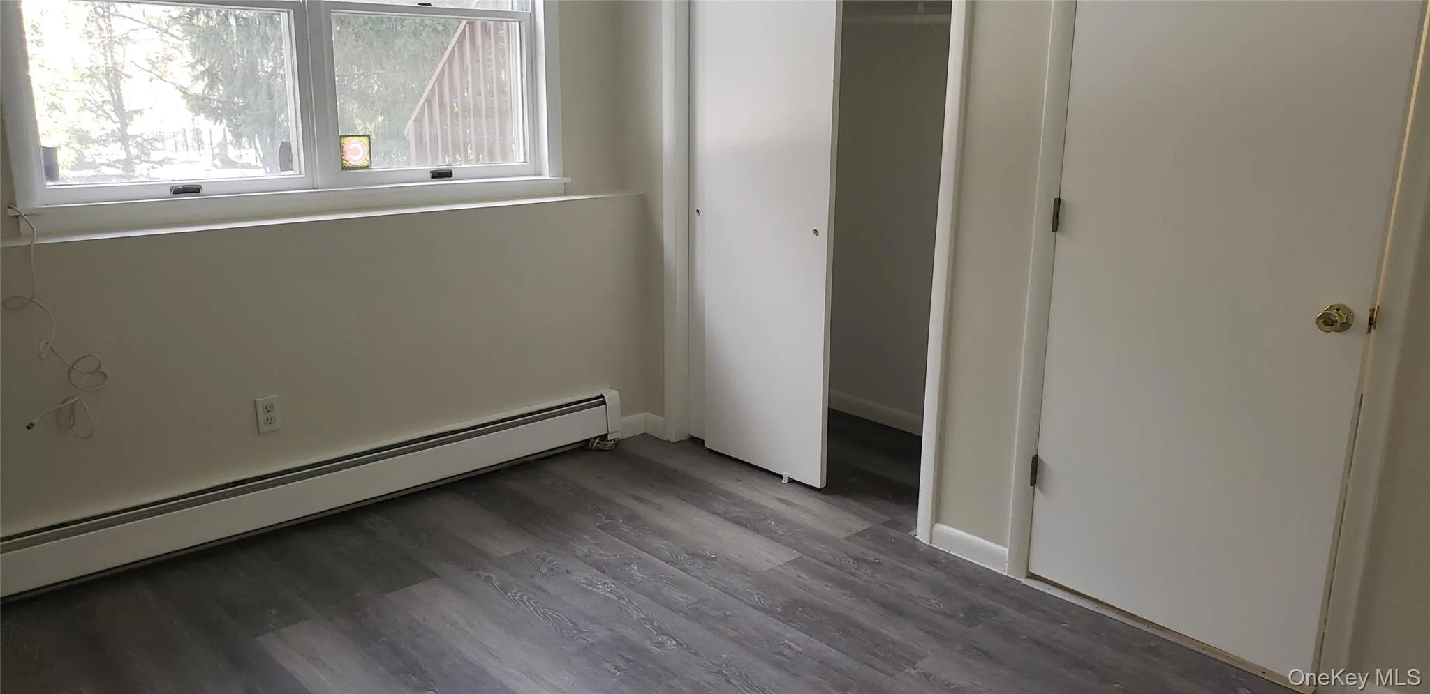 Unfurnished bedroom with baseboard heating, wood finished floors, and a closet Unfurnished bedroom with baseboard heating, wood finished floors, and a closet