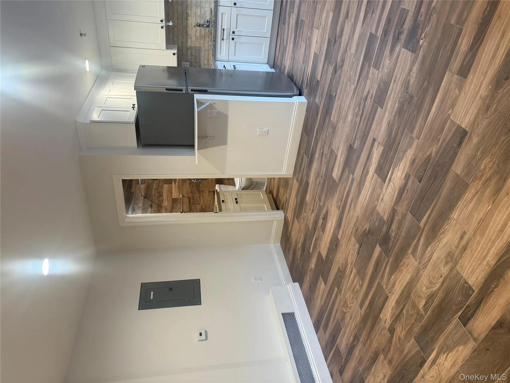 Kitchen with white cabinetry, dark wood-type flooring, refrigerator, electric panel, and light stone counters Kitchen with white cabinetry, dark wood-type flooring, refrigerator, electric panel, and light stone counters