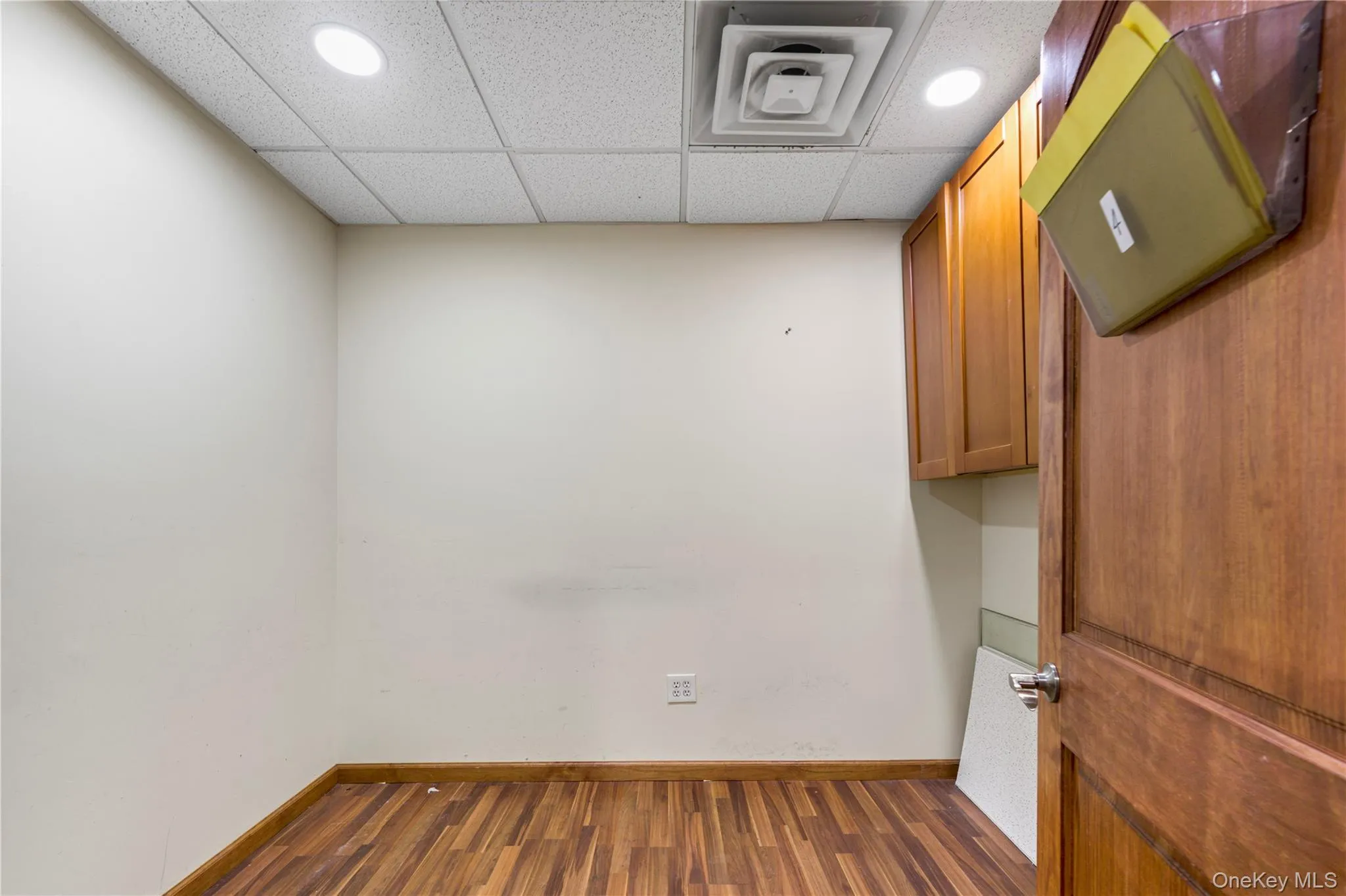 Empty room with a paneled ceiling, dark wood-type flooring, and recessed lighting Empty room with a paneled ceiling, dark wood-type flooring, and recessed lighting