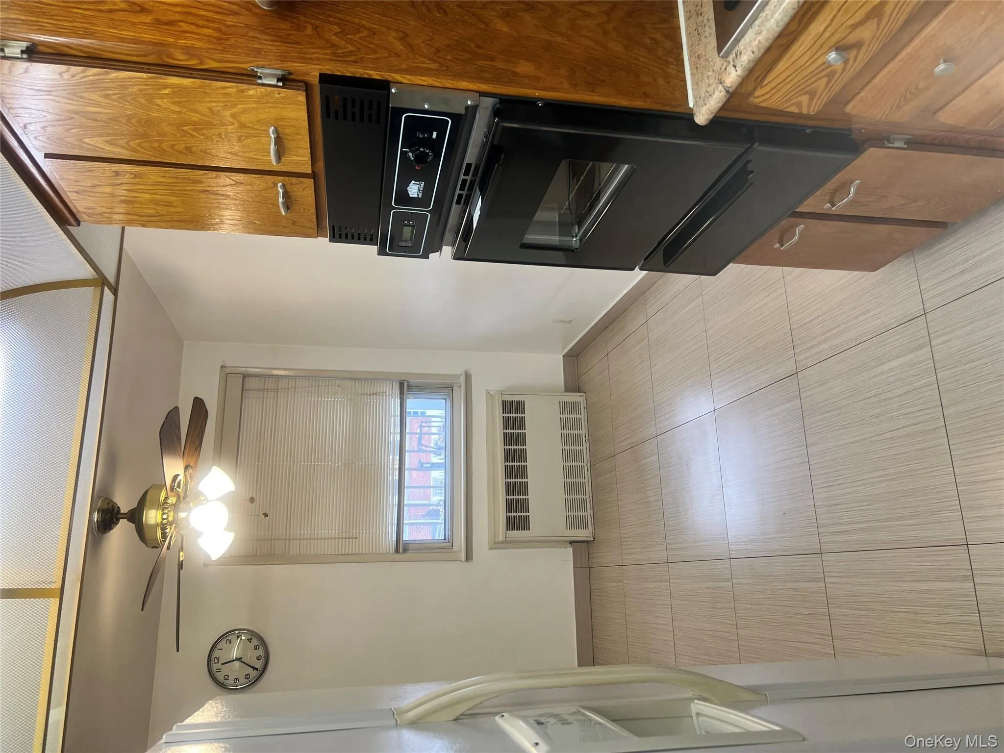 Kitchen featuring brown cabinets, fridge, a warming drawer, ceiling fan, and radiator heating unit Kitchen featuring brown cabinets, fridge, a warming drawer, ceiling fan, and radiator heating unit
