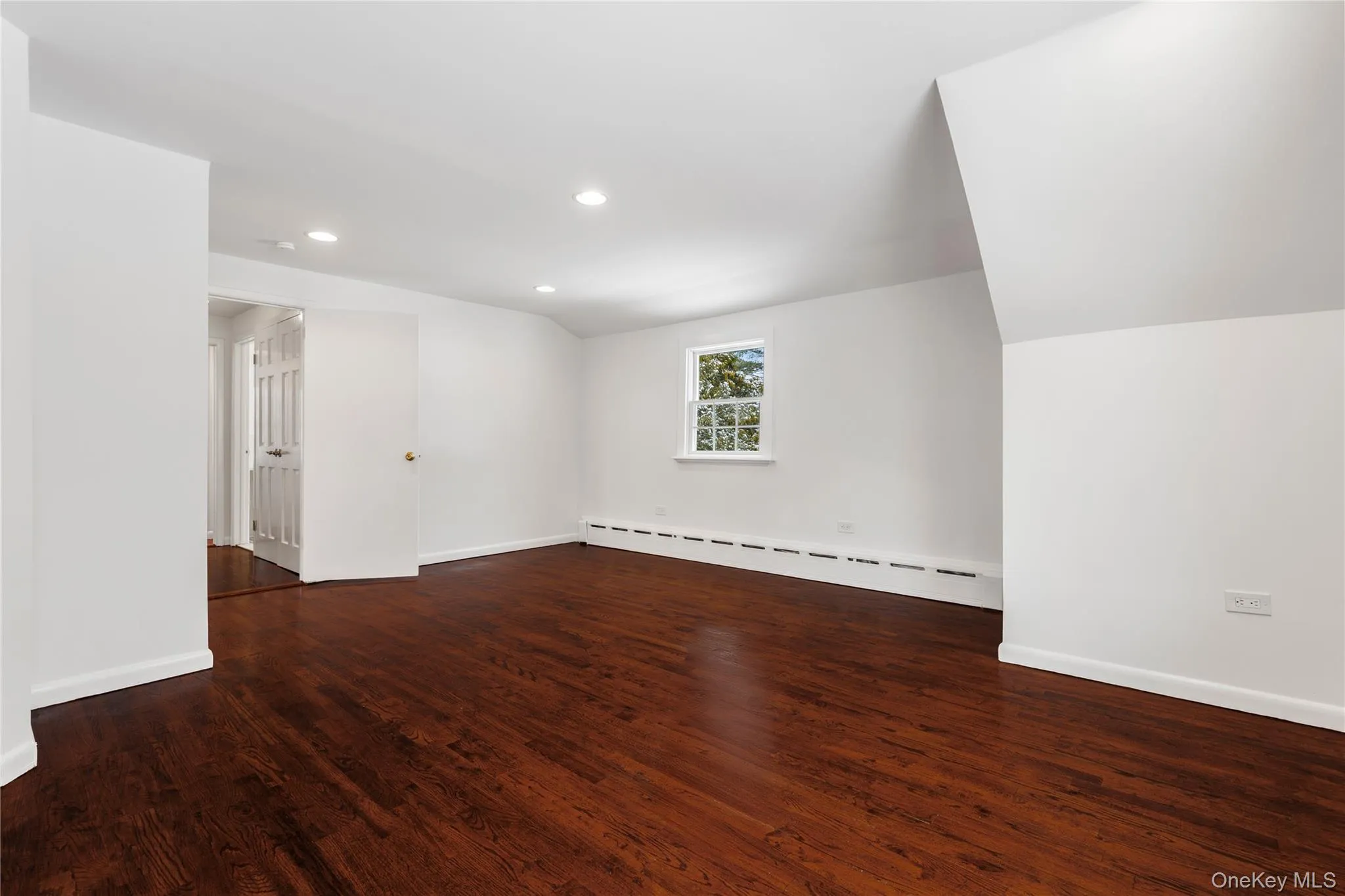 Empty room featuring lofted ceiling, recessed lighting, baseboard heating, and dark wood-type flooring Empty room featuring lofted ceiling, recessed lighting, baseboard heating, and dark wood-type flooring