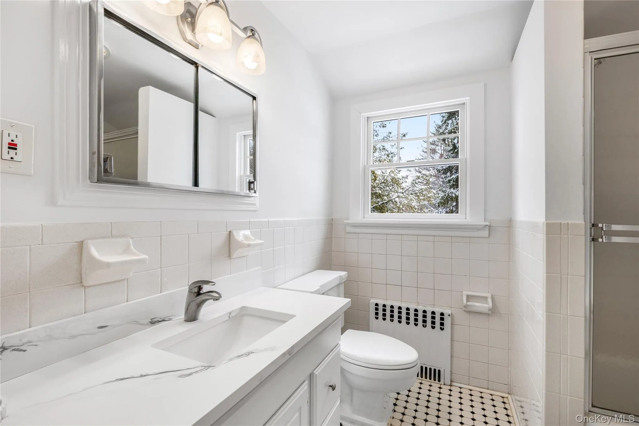 Full bathroom with radiator, vanity, a shower stall, tile walls, and wainscoting Full bathroom with radiator, vanity, a shower stall, tile walls, and wainscoting