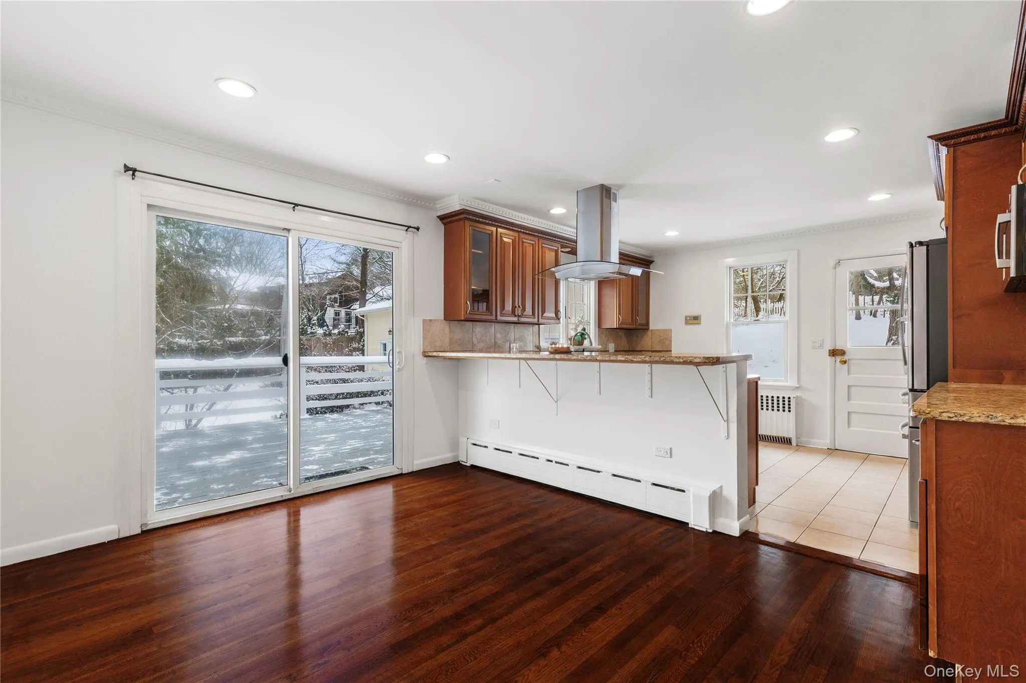 Kitchen with brown cabinetry, a kitchen breakfast bar, dark wood finished floors, a baseboard radiator, and island exhaust hood Kitchen with brown cabinetry, a kitchen breakfast bar, dark wood finished floors, a baseboard radiator, and island exhaust hood