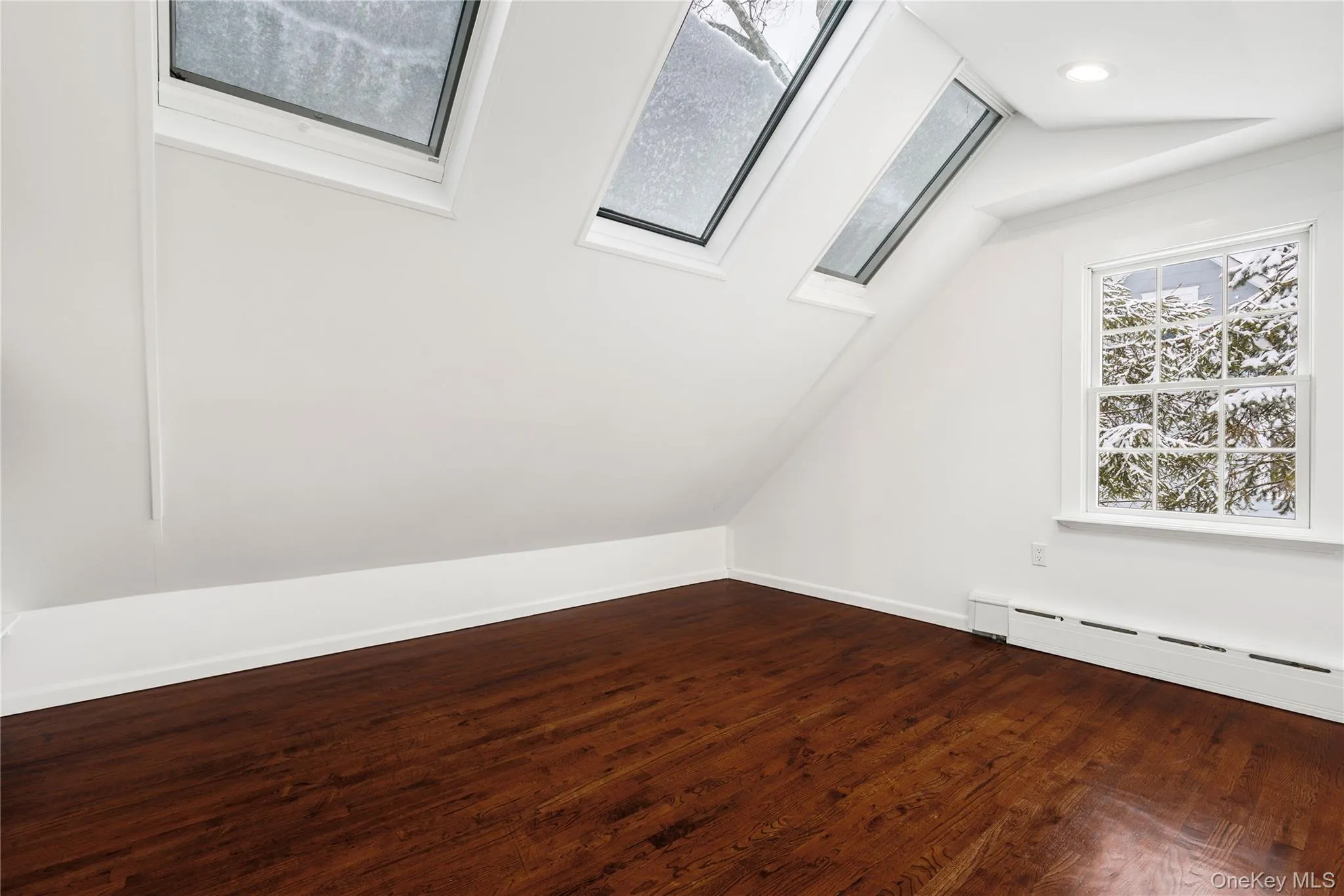 Bonus room with lofted ceiling, dark wood-style floors, a skylight, and a baseboard heating unit Bonus room with lofted ceiling, dark wood-style floors, a skylight, and a baseboard heating unit