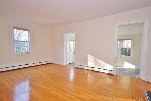Unfurnished room with light wood-type flooring, a baseboard heating unit, healthy amount of natural light, and crown molding Unfurnished room with light wood-type flooring, a baseboard heating unit, healthy amount of natural light, and crown molding
