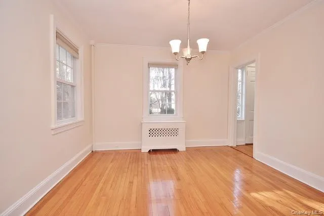 Unfurnished dining area featuring radiator heating unit, light wood-style floors, crown molding, plenty of natural light, and a chandelier Unfurnished dining area featuring radiator heating unit, light wood-style floors, crown molding, plenty of natural light, and a chandelier