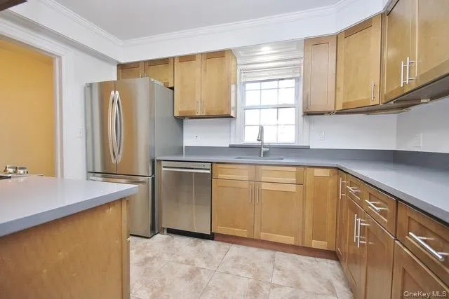 Kitchen with brown cabinetry, appliances with stainless steel finishes, ornamental molding, and light tile patterned flooring Kitchen with brown cabinetry, appliances with stainless steel finishes, ornamental molding, and light tile patterned flooring