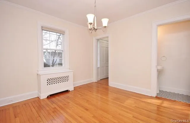 Unfurnished dining area with radiator, light wood-type flooring, a chandelier, and ornamental molding Unfurnished dining area with radiator, light wood-type flooring, a chandelier, and ornamental molding