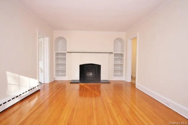 Unfurnished living room featuring a fireplace with raised hearth, light wood-type flooring, ornamental molding, and a baseboard radiator Unfurnished living room featuring a fireplace with raised hearth, light wood-type flooring, ornamental molding, and a baseboard radiator