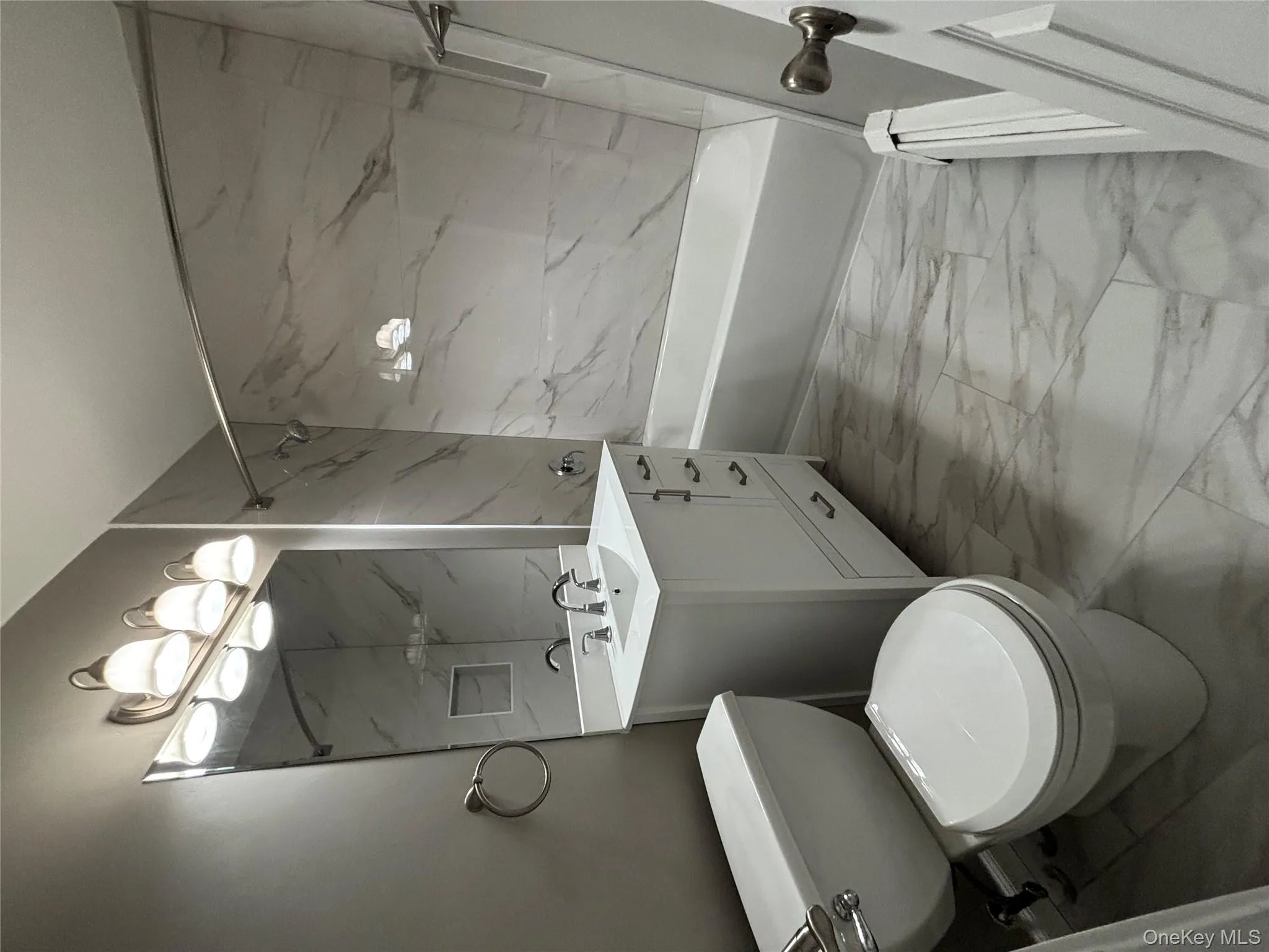 Full bathroom with light marble finish flooring, vanity, a combined bath / shower with marble appearance, and baseboard heating Full bathroom with light marble finish flooring, vanity, a combined bath / shower with marble appearance, and baseboard heating