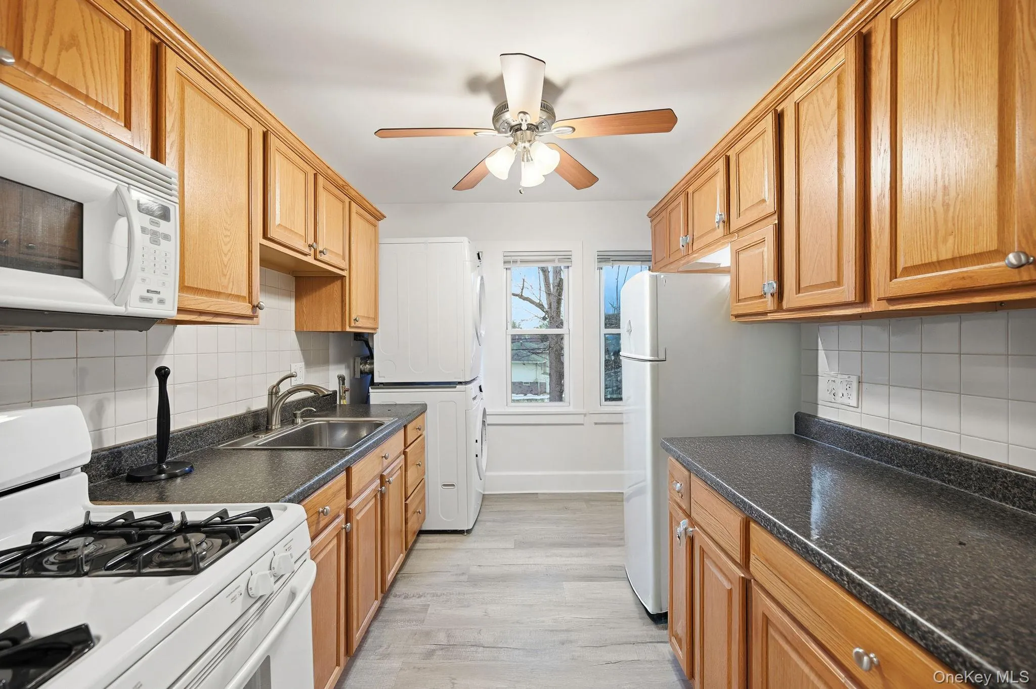 Kitchen featuring white appliances, ceiling fan, dark countertops, and backsplash Kitchen featuring white appliances, ceiling fan, dark countertops, and backsplash