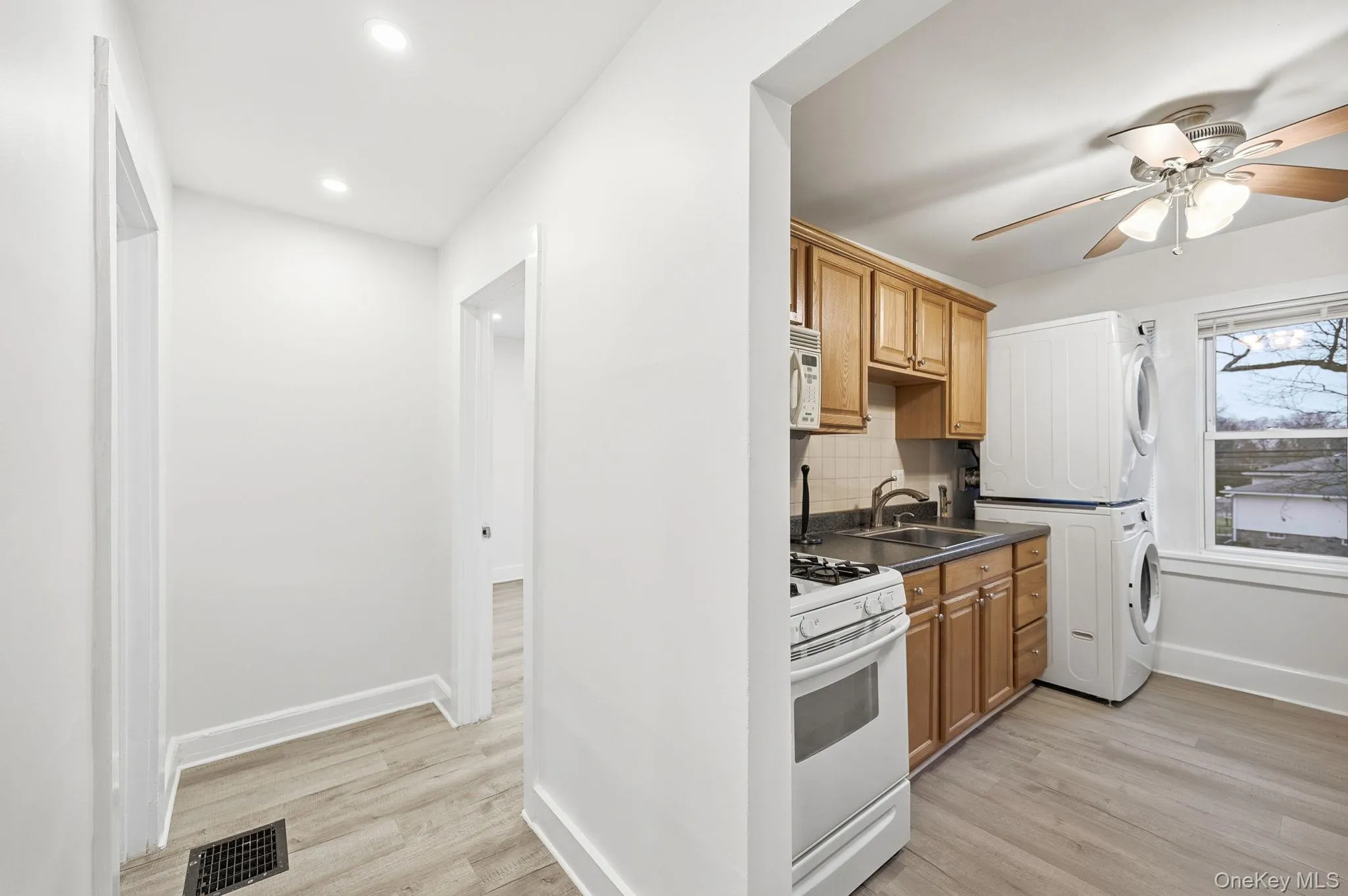 Kitchen with dark countertops, light wood-type flooring, white appliances, tasteful backsplash, and recessed lighting Kitchen with dark countertops, light wood-type flooring, white appliances, tasteful backsplash, and recessed lighting