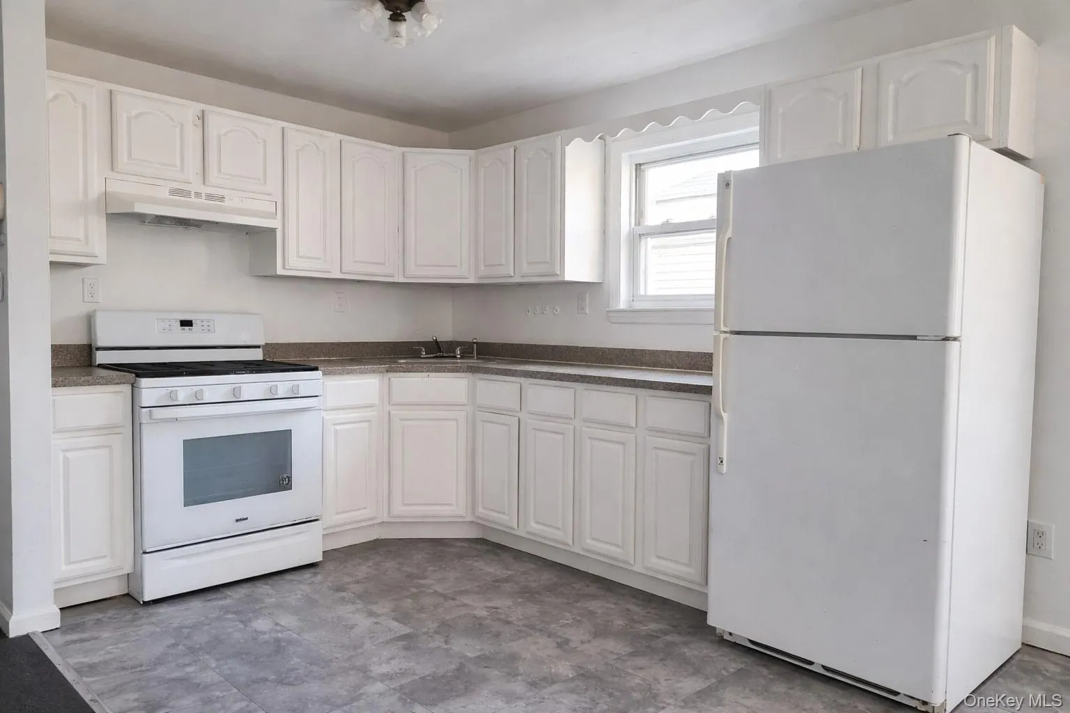 Kitchen featuring white appliances, white cabinetry, under cabinet range hood, dark countertops, and light floors Kitchen featuring white appliances, white cabinetry, under cabinet range hood, dark countertops, and light floors