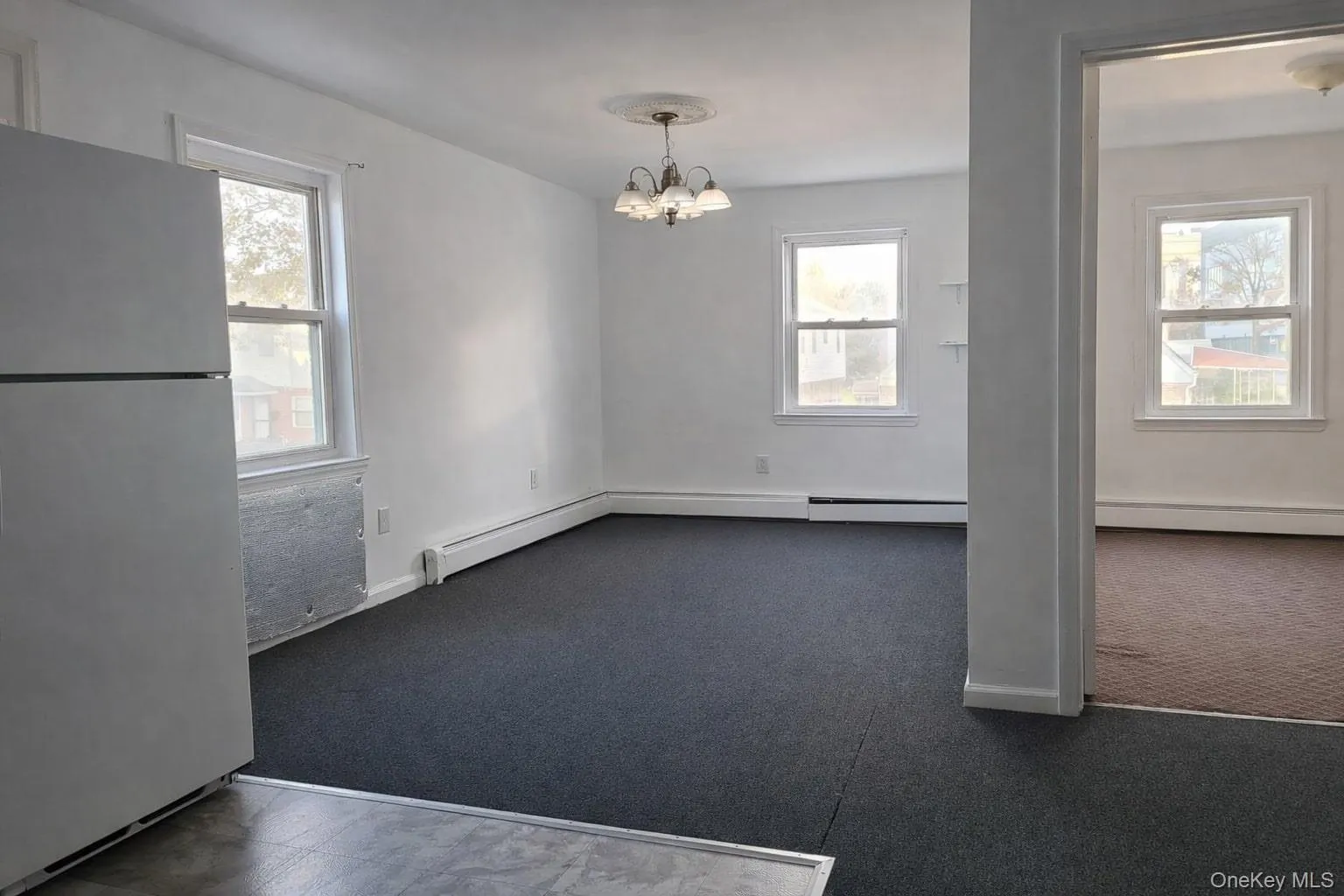 Empty room with a baseboard heating unit, a chandelier, and dark carpet Empty room with a baseboard heating unit, a chandelier, and dark carpet