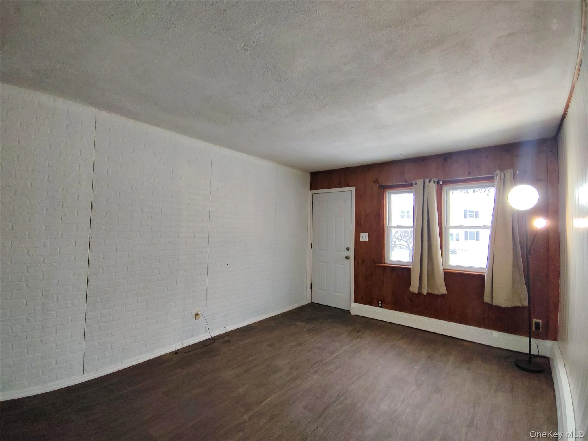 Unfurnished room featuring dark wood-style flooring, a textured ceiling, and a baseboard radiator Unfurnished room featuring dark wood-style flooring, a textured ceiling, and a baseboard radiator