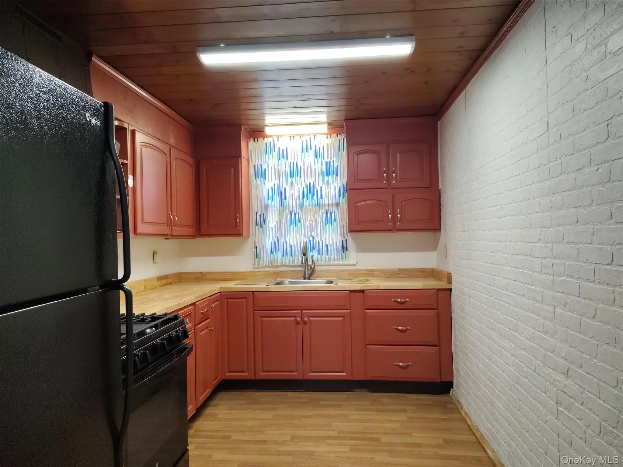 Kitchen with brick wall, black appliances, light countertops, light wood finished floors, and wood ceiling Kitchen with brick wall, black appliances, light countertops, light wood finished floors, and wood ceiling