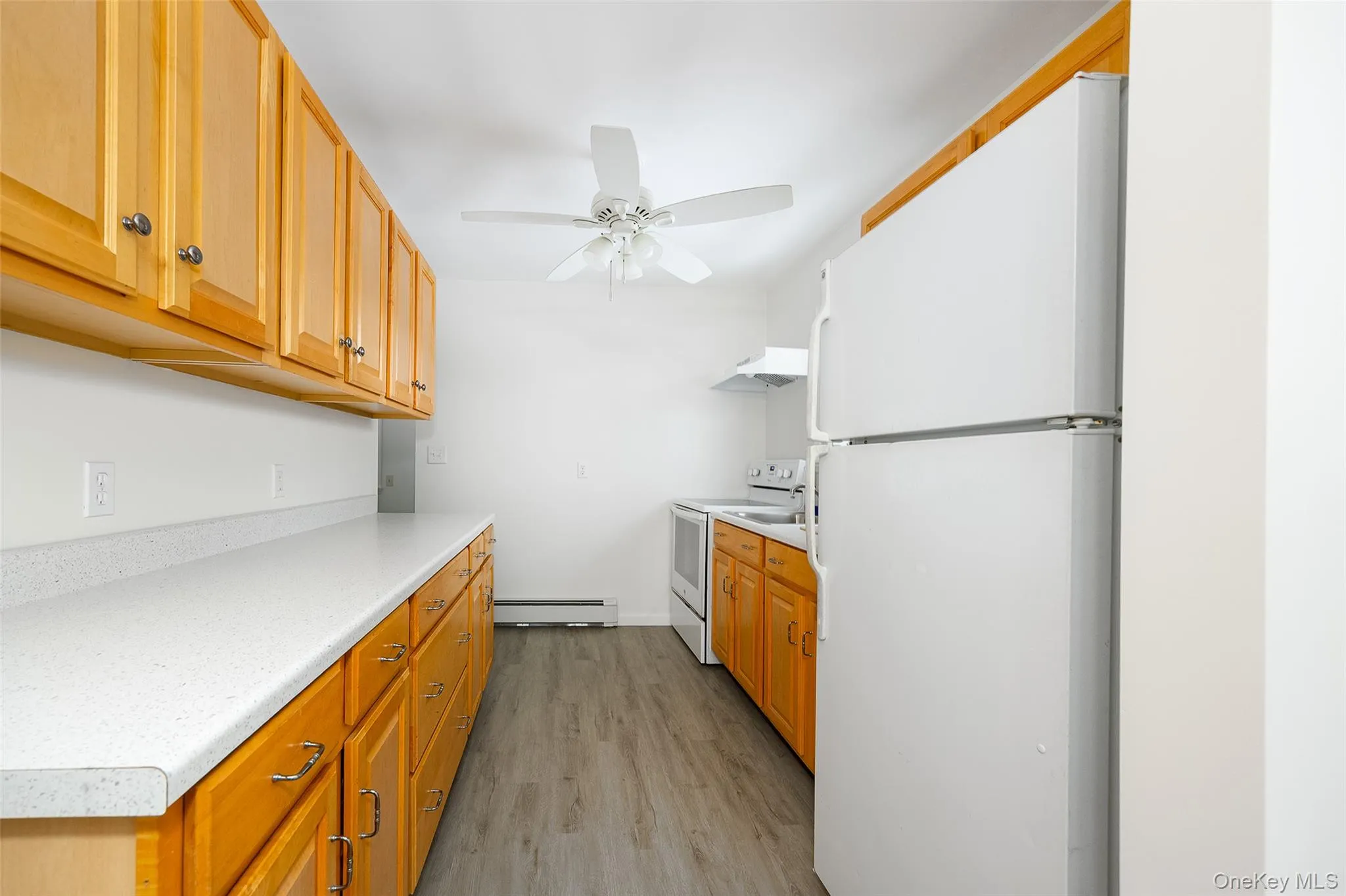 Kitchen featuring white appliances, light countertops, light wood-style flooring, under cabinet range hood, and a baseboard radiator Kitchen featuring white appliances, light countertops, light wood-style flooring, under cabinet range hood, and a baseboard radiator
