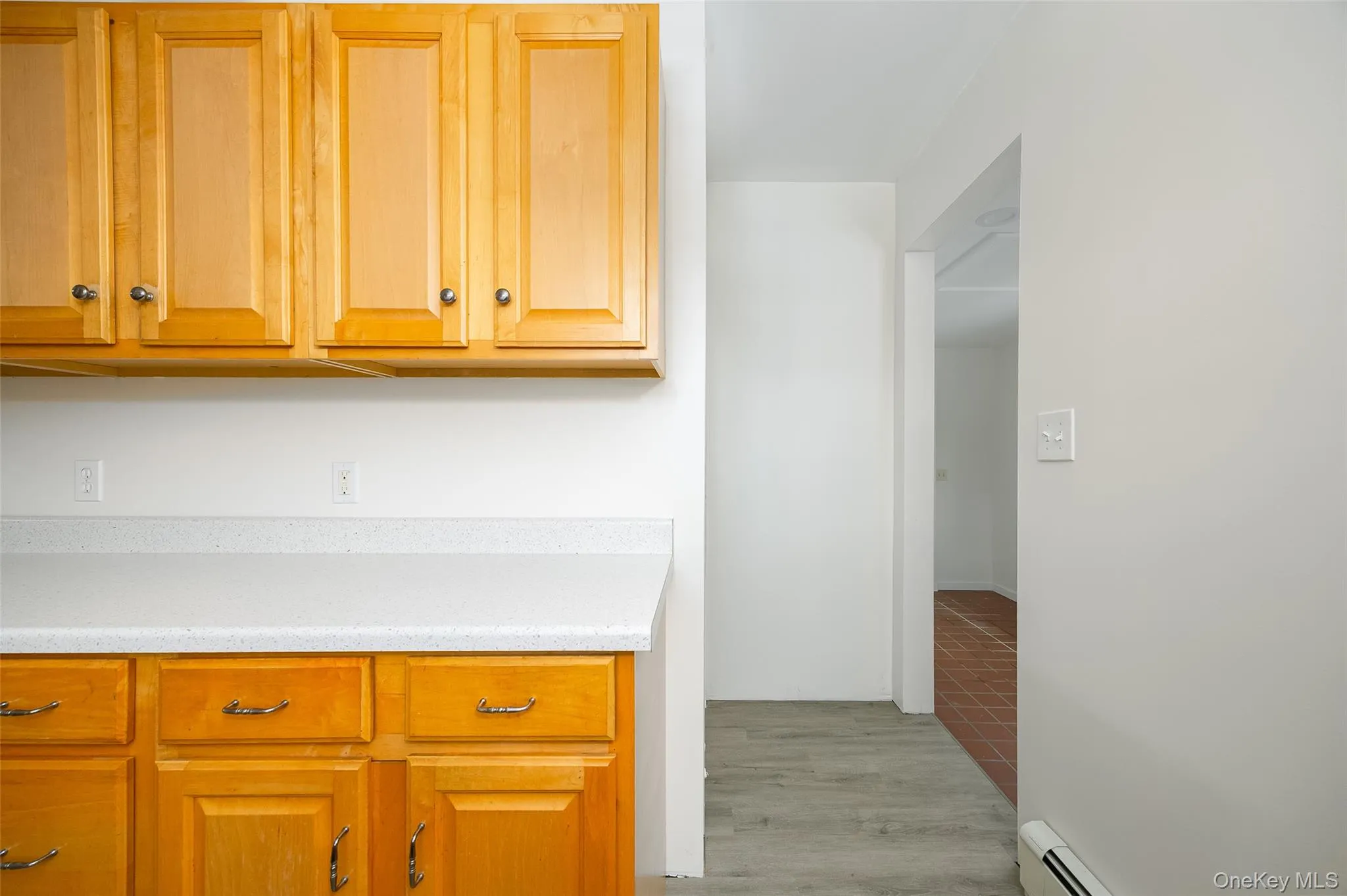 Kitchen featuring a baseboard heating unit, light stone countertops, light wood-type flooring, and brown cabinets Kitchen featuring a baseboard heating unit, light stone countertops, light wood-type flooring, and brown cabinets