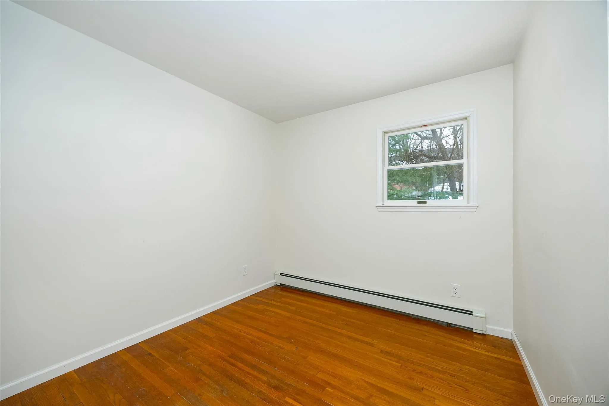 Unfurnished room featuring baseboard heating and hardwood / wood-style flooring Unfurnished room featuring baseboard heating and hardwood / wood-style flooring