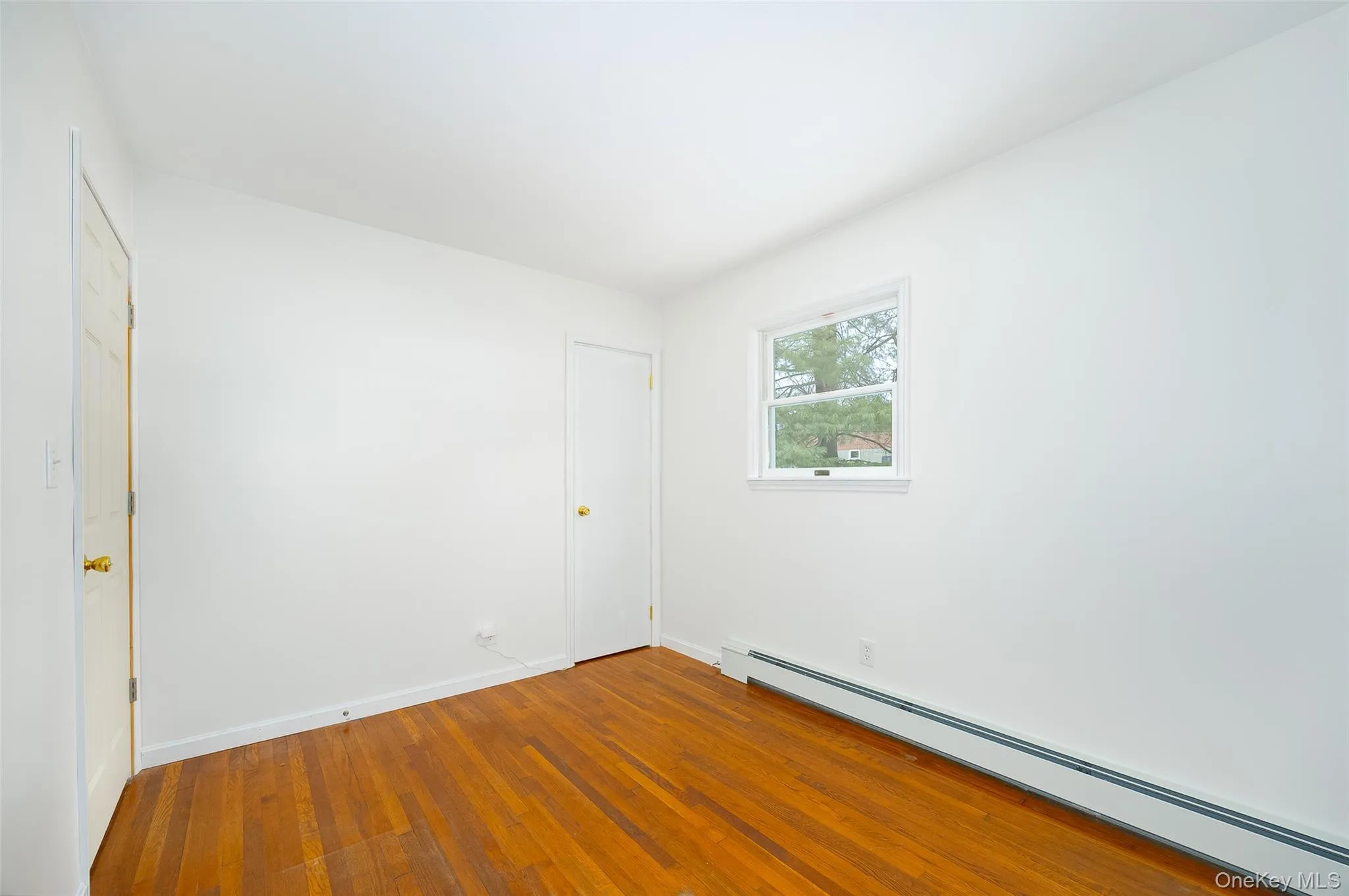 Unfurnished bedroom featuring baseboard heating and hardwood / wood-style flooring Unfurnished bedroom featuring baseboard heating and hardwood / wood-style flooring