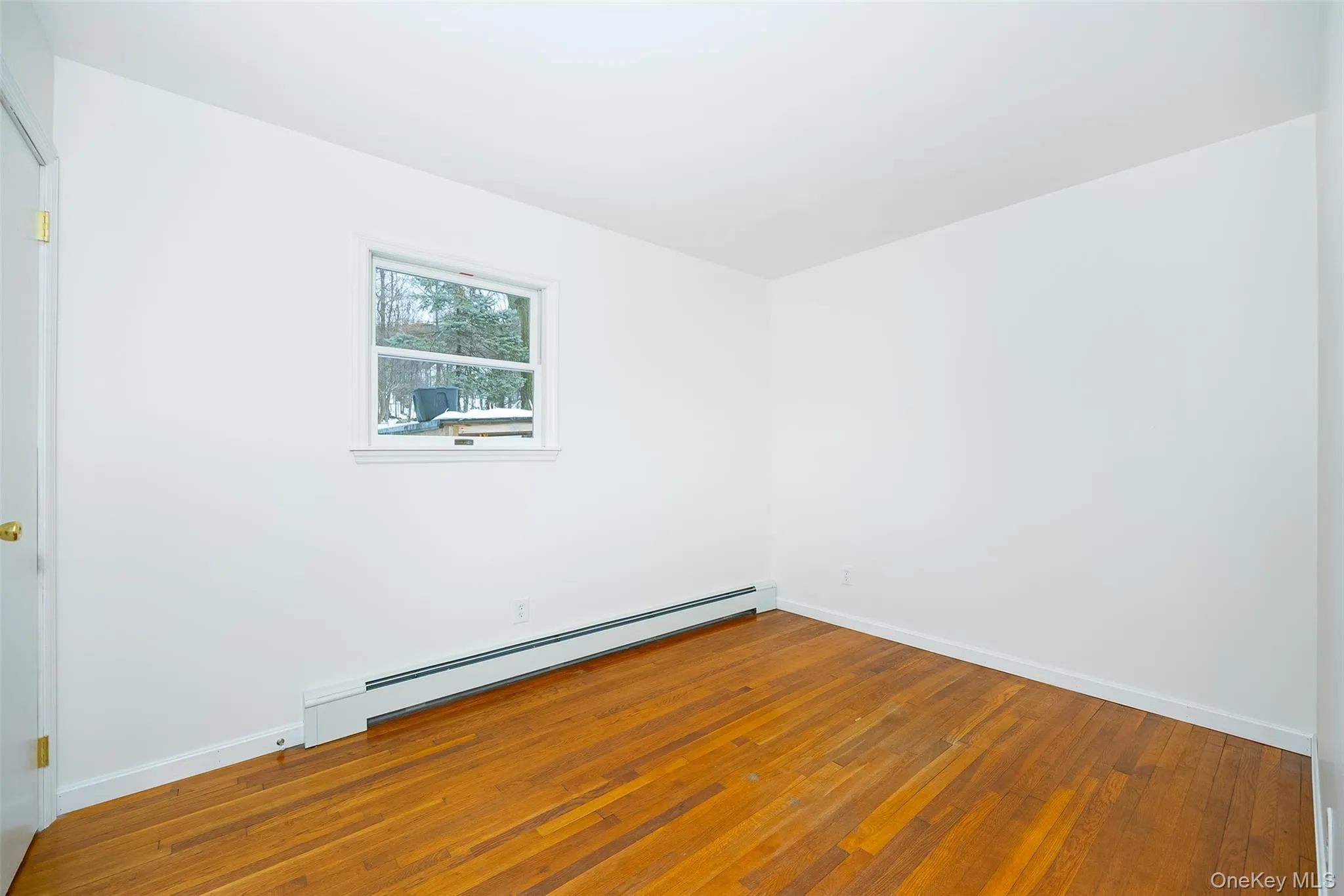 Unfurnished room with a baseboard radiator and hardwood / wood-style floors Unfurnished room with a baseboard radiator and hardwood / wood-style floors