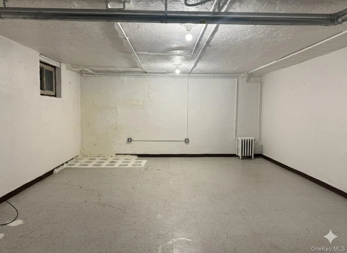 Basement featuring light flooring, radiator, and a textured wall Basement featuring light flooring, radiator, and a textured wall