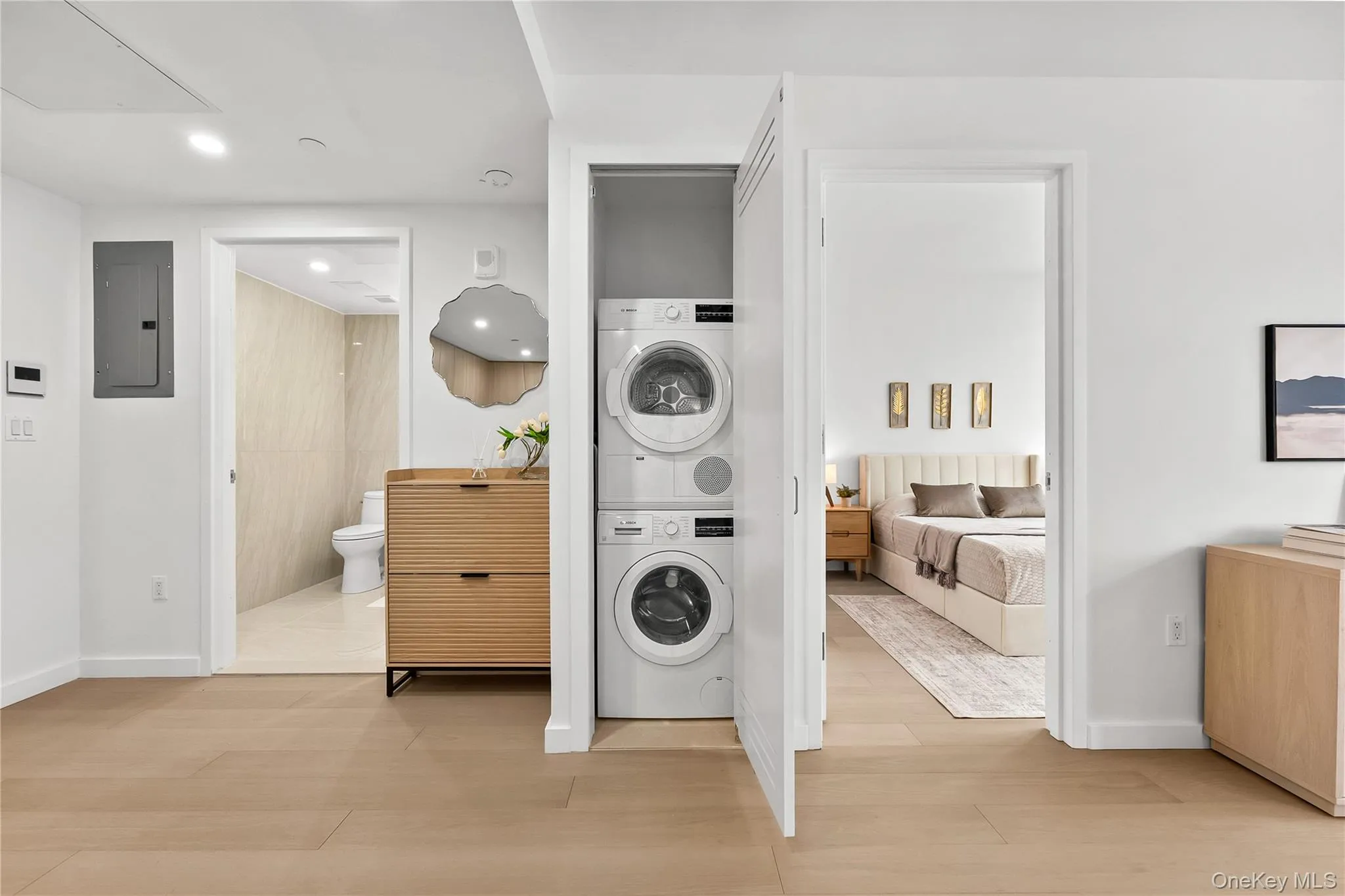 Laundry area featuring electric panel, stacked washer and clothes dryer, light wood-type flooring, and recessed lighting Laundry area featuring electric panel, stacked washer and clothes dryer, light wood-type flooring, and recessed lighting