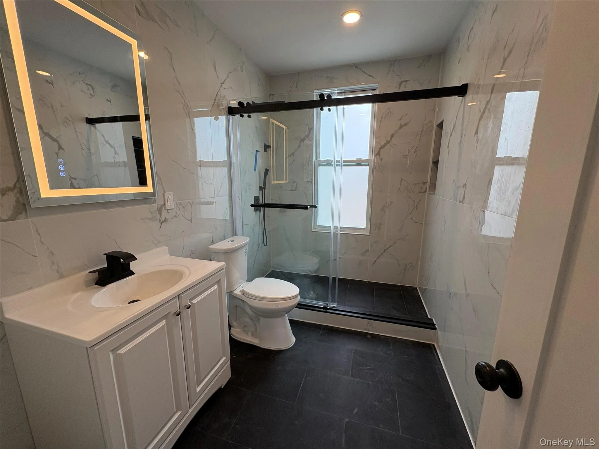 Full bathroom featuring vanity, a marble finish shower, a baseboard radiator, tile walls, and stone wall Full bathroom featuring vanity, a marble finish shower, a baseboard radiator, tile walls, and stone wall